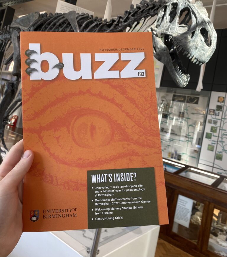 The front cover of Buzz Magazine, Nov-Dec 2022, being held up in front of a large dinosaur skeleton.